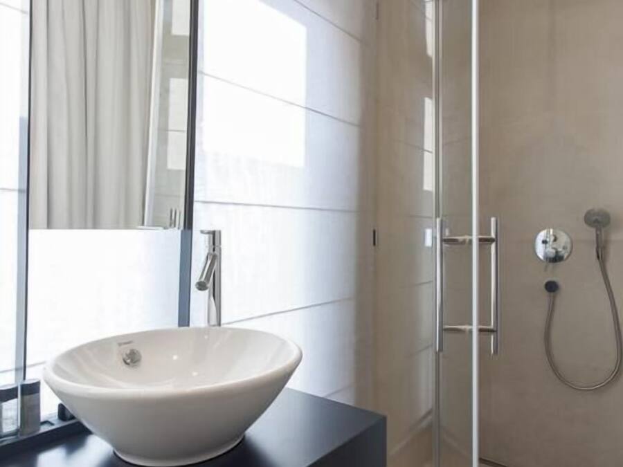 A modern bathroom with a large mirror, a white vessel sink, and a glass-enclosed shower area.