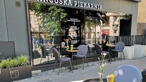 Un espace extérieur aménagé avec des tables et des chaises, situé devant la devanture d’une boutique appelée « Francuska Piekarnia ».