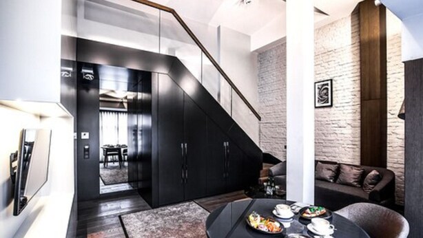 Un espace de vie moderne comprenant un escalier, un parquet en bois foncé, une table basse ronde sur laquelle se trouvent des aliments, un canapé et un mur en briques.