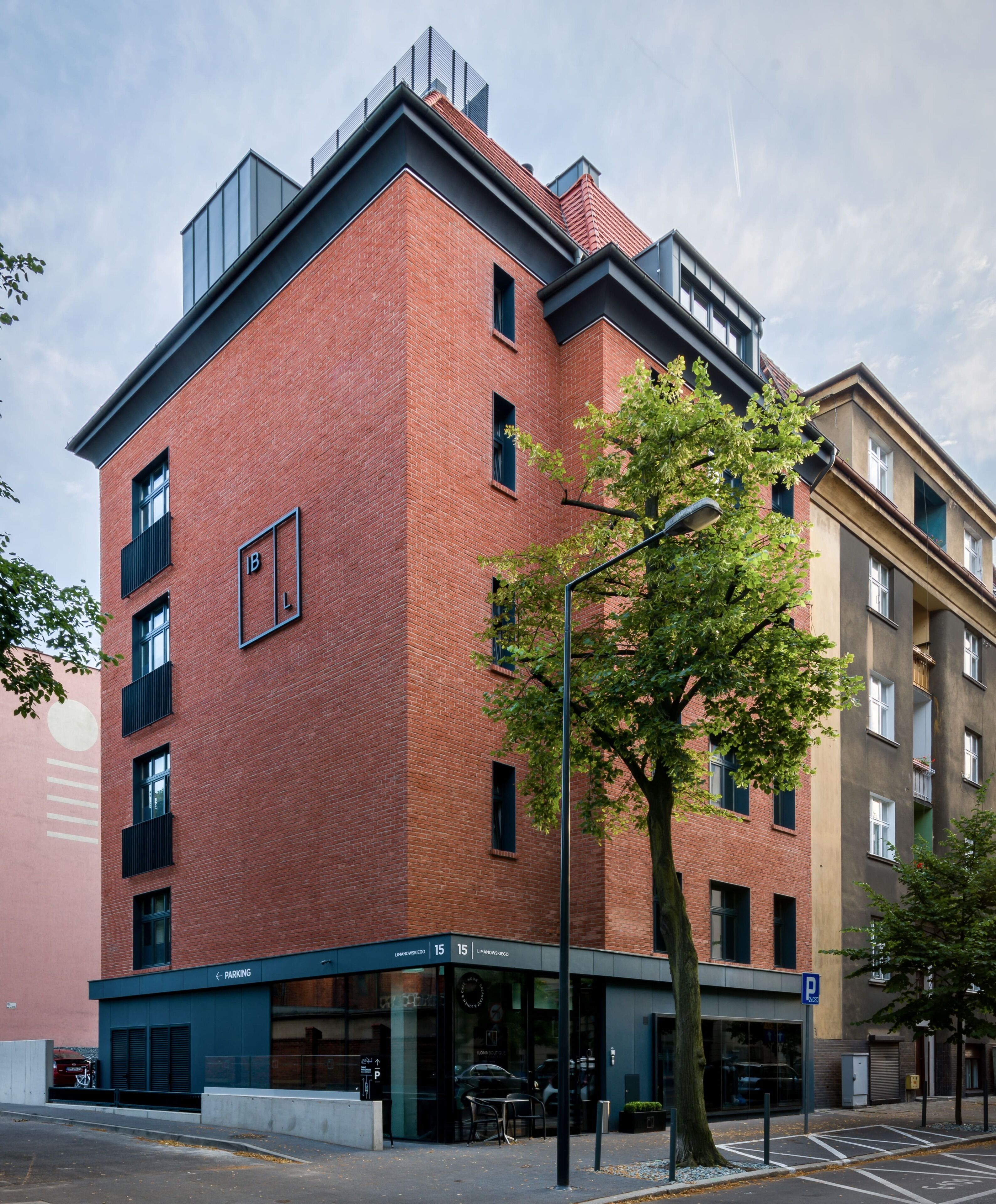 A multi-story building with a red brick facade, a visible parking sign, and a tree in front.