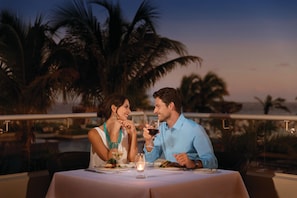 A couple dining at an outdoor table with a view of palm trees and a sunset. - Turquoize at Hyatt Ziva Cancun - Adults Only - All Inclusive (Cancun)