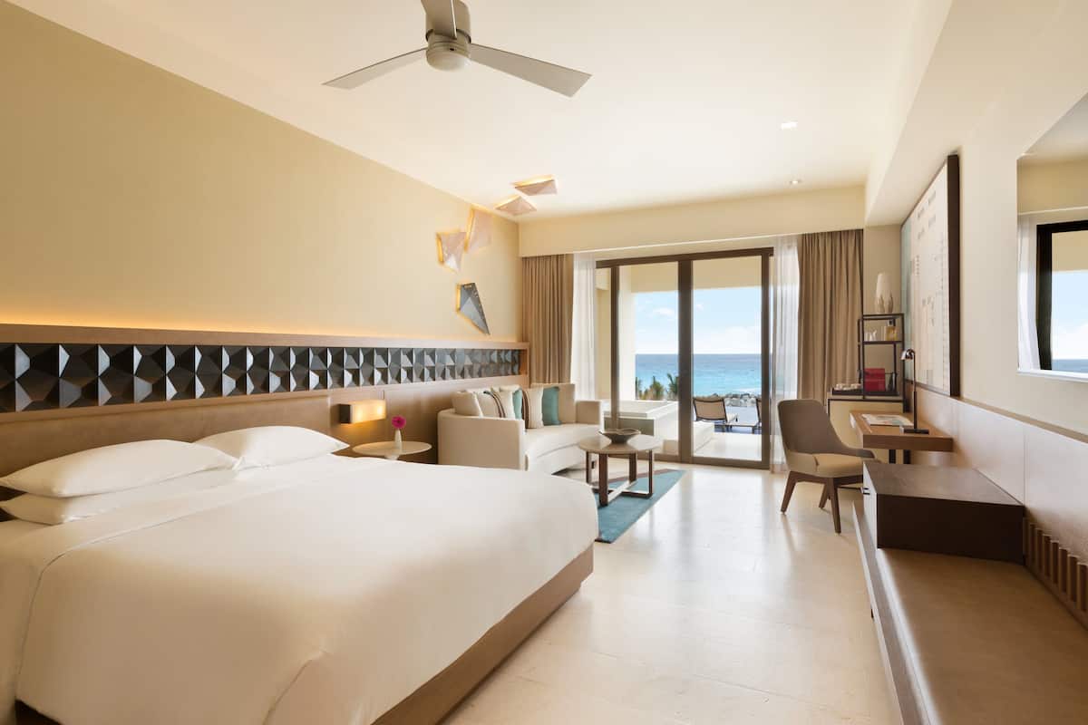 A hotel room with a large bed, a desk, a chair, a sofa, and a view of the ocean.