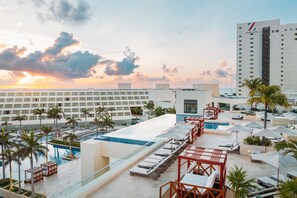 A rooftop pool area with lounge chairs, umbrellas, and palm trees.