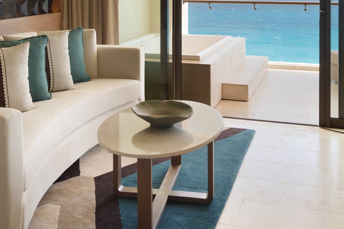 A modern hotel room with a balcony, a sofa, a coffee table, and a view of the ocean.