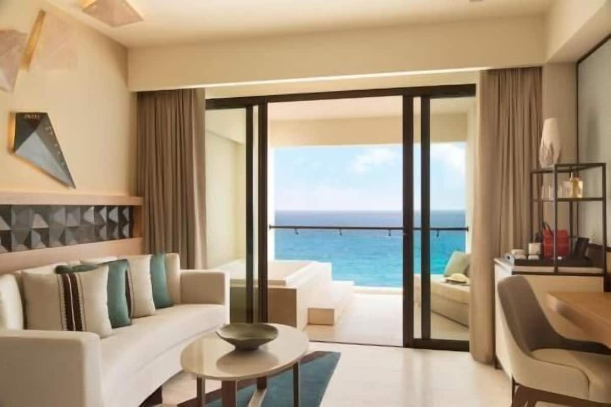 A modern hotel room with a balcony, a sofa, a coffee table, and a view of the ocean.