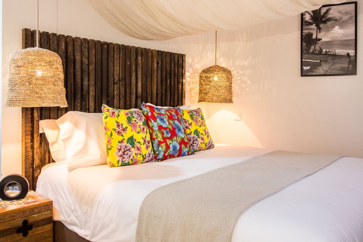 A bedroom with a bed, pillows, a bedside table, and a wall-mounted lamp.