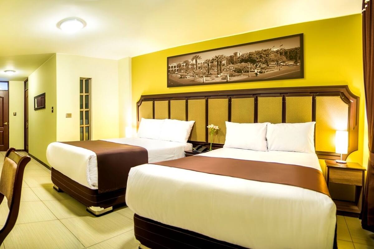 Une chambre d’hôtel avec deux lits, un bureau, une chaise et un tableau au mur.