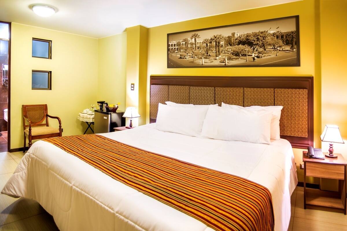 Une chambre d’hôtel avec un grand lit, une chaise, une petite table, une table de chevet et un tableau au mur.