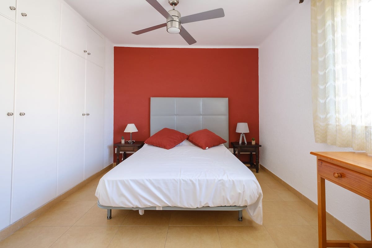 A bedroom with a bed, two bedside tables with lamps, a ceiling fan, and a wooden nightstand.