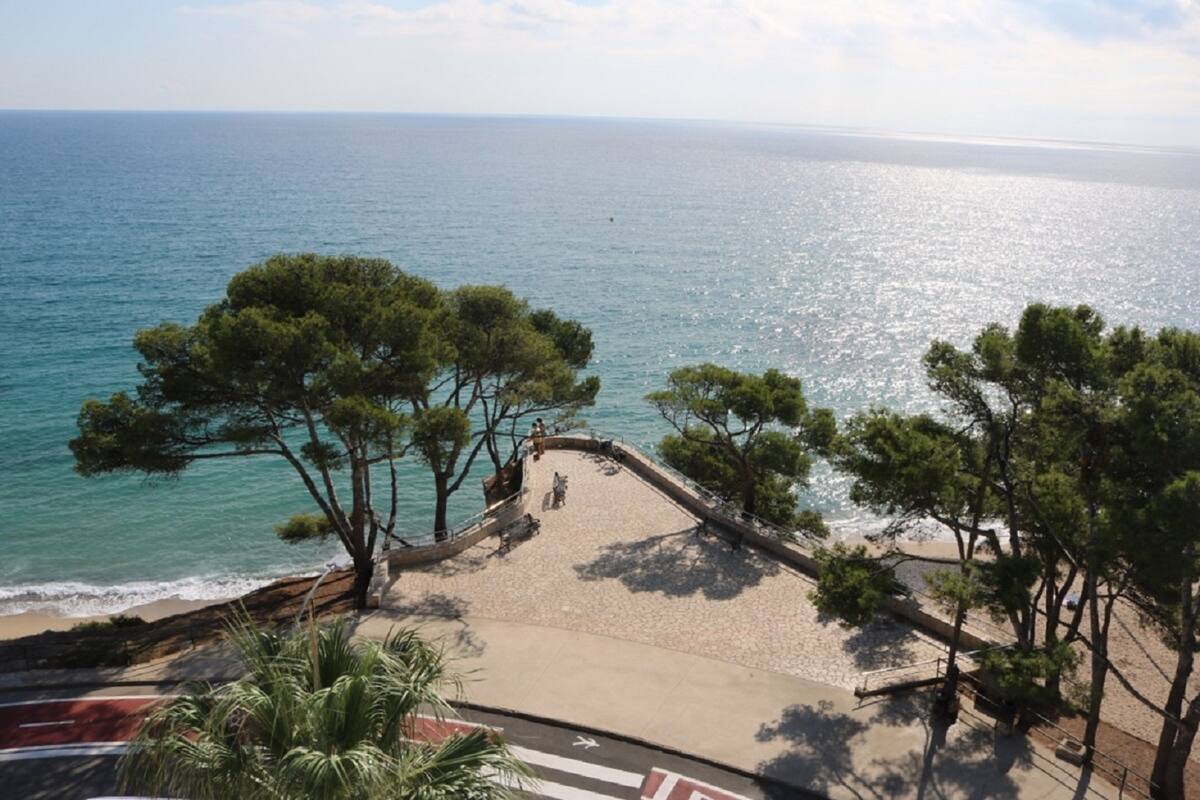 A coastal promenade with a beach, trees, and a view of the sea.