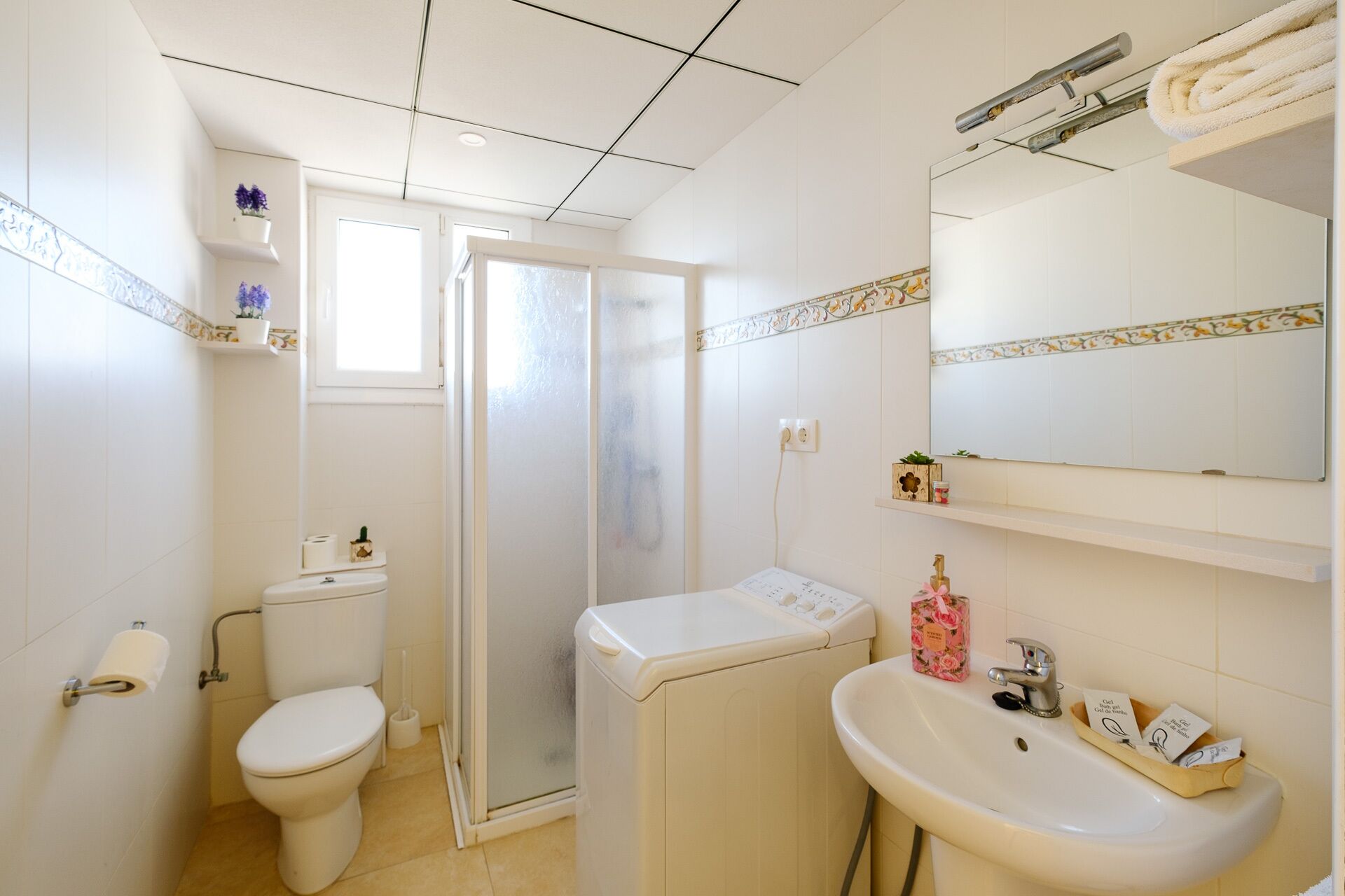 A compact bathroom with a toilet, a washing machine, a sink, and a shower.