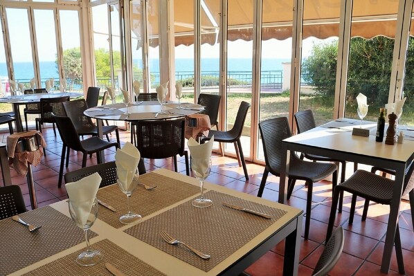 Een restaurant met terras, tafels gedekt met witte servetten en wijnglazen, en uitzicht op zee.