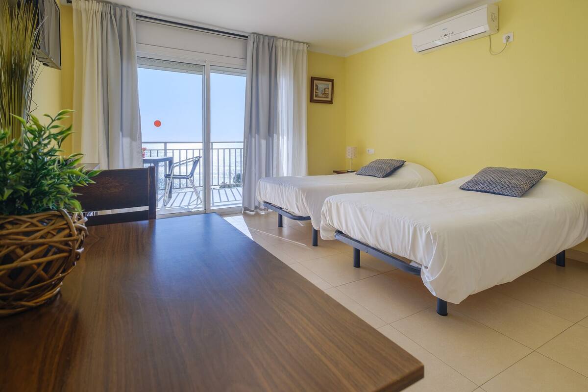 A hotel room with two beds, a dining table, a chair, and a balcony with a view.