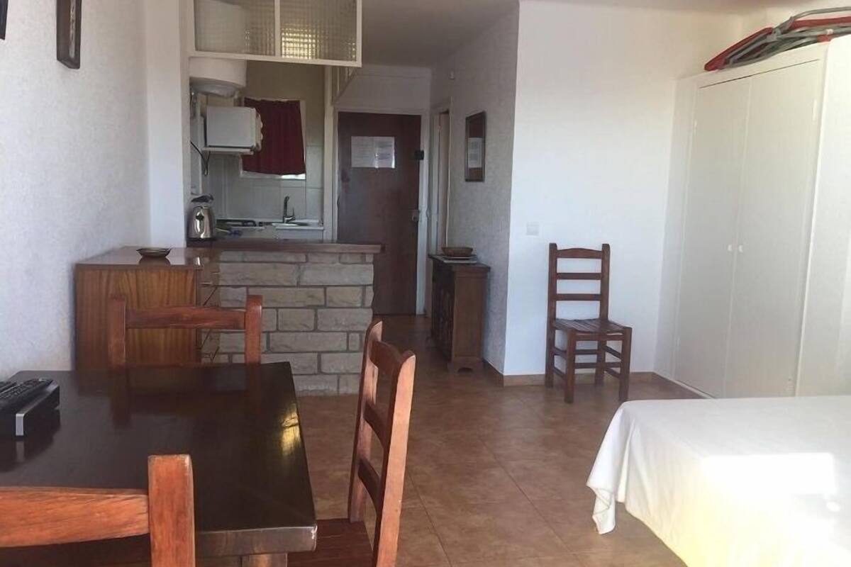 A compact kitchen with a stone countertop, a dining area with a wooden table and chairs, and a white wardrobe.
