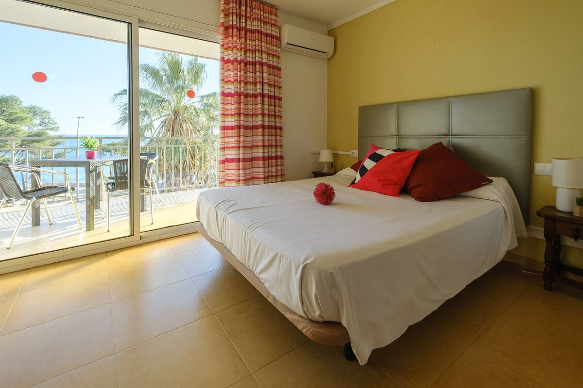 A hotel room with a bed, a balcony with a table and chairs, and a view of palm trees.
