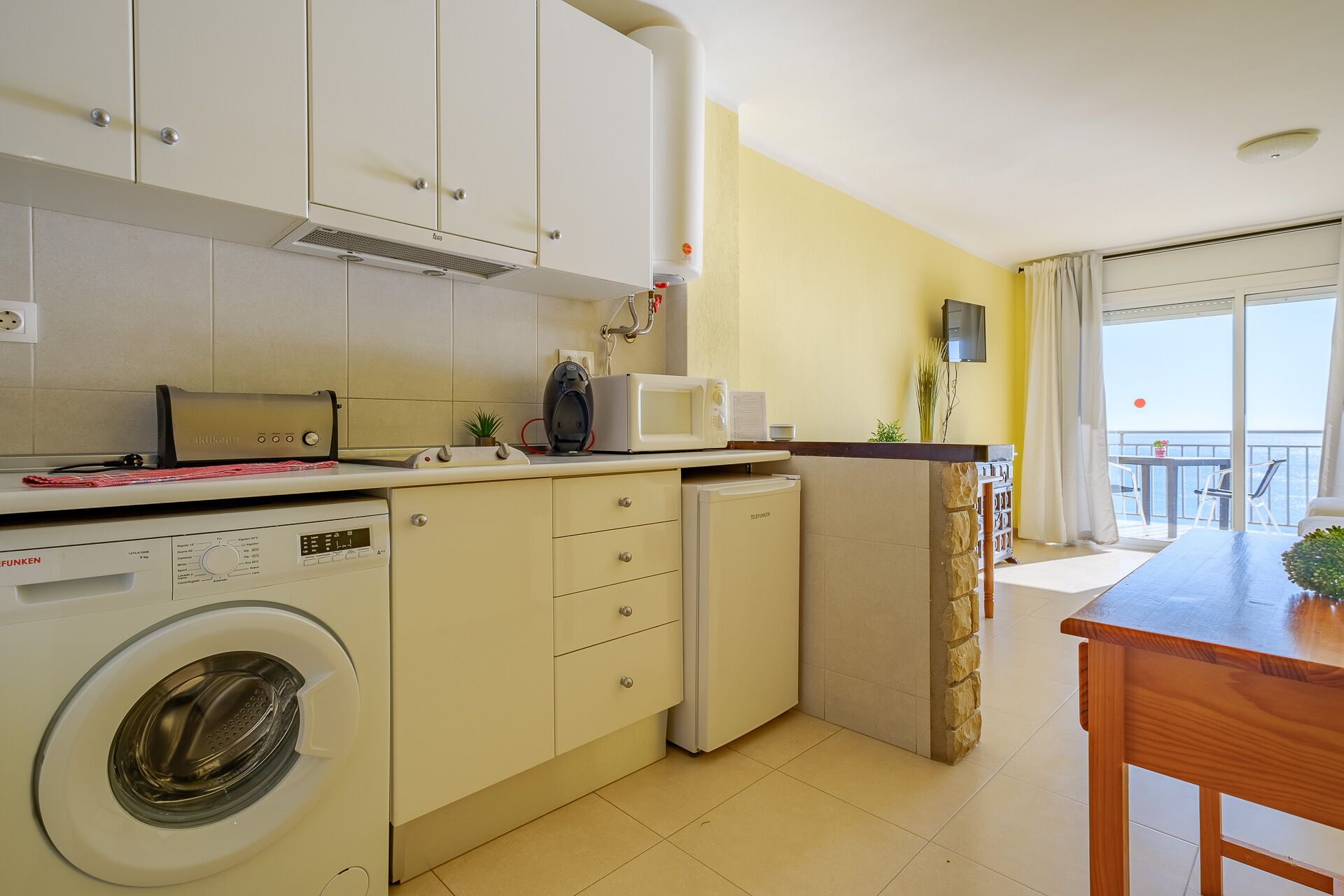 Una cocina funcional con lavadora, microondas y un refrigerador pequeño.