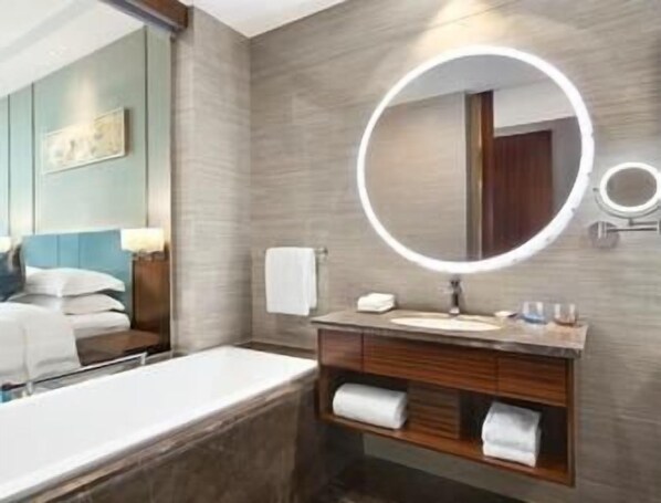 Un baño moderno con un espejo grande, una bañera y un tocador con toallero.