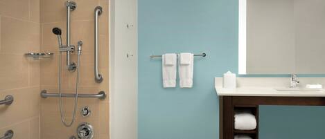 A bathroom with a shower, grab bars, a sink, and a towel rack.