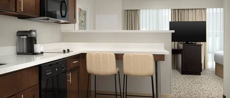 A modern kitchen with a microwave, coffee maker, and bar stools.