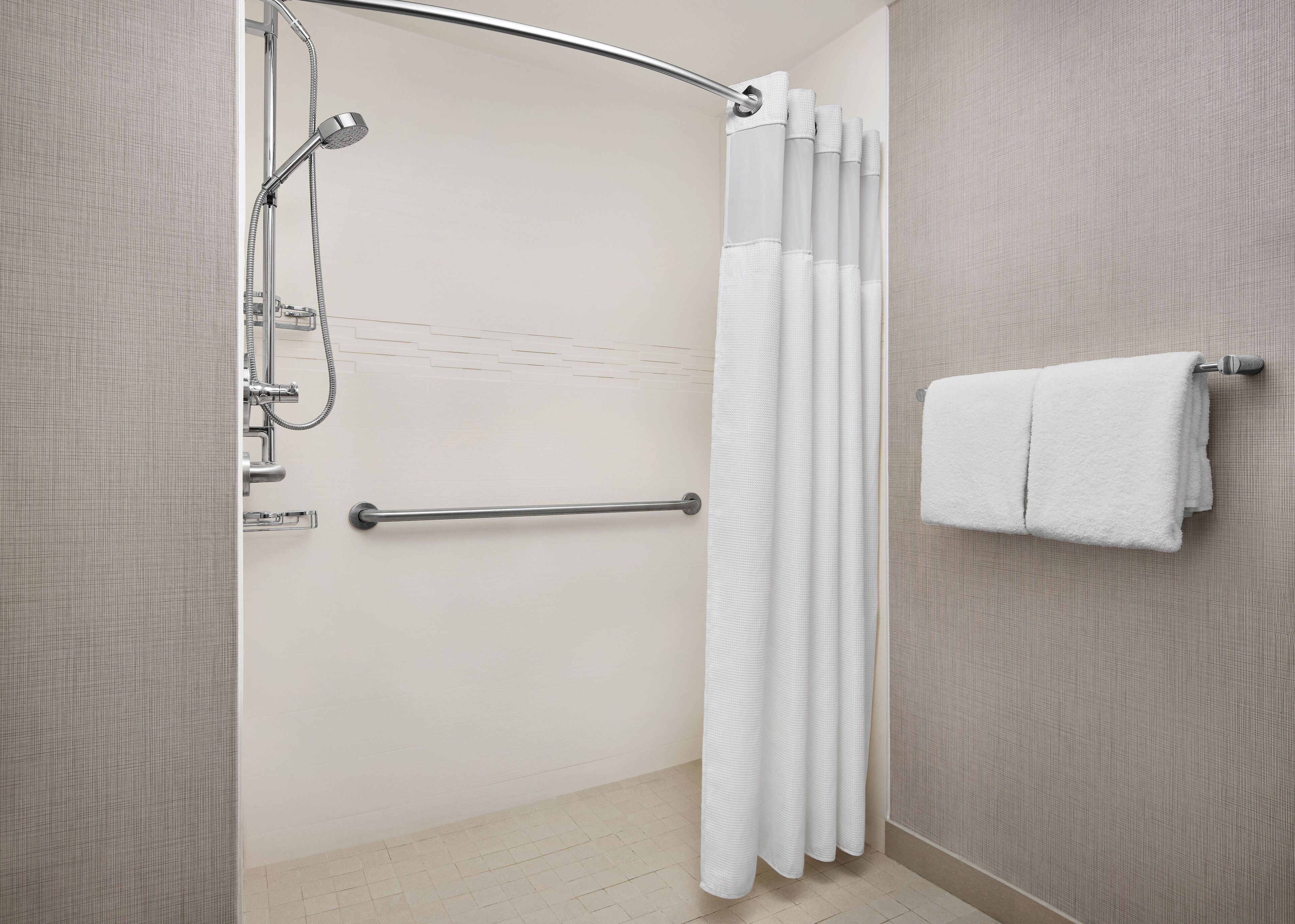 A modern bathroom with a shower, a handrail, a towel rack, and a textured wall.
