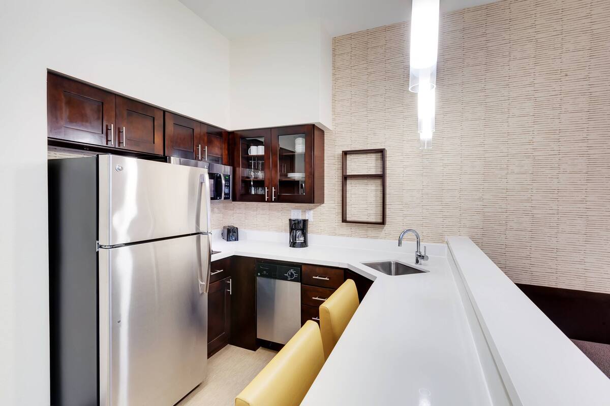 A modern kitchen with stainless steel appliances, dark wooden cabinets, and a white countertop.