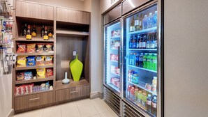 A kitchenette with a refrigerator stocked with beverages and snacks, and shelves with packaged food items. - Residence Inn by Marriott Austin Airport (Austin)