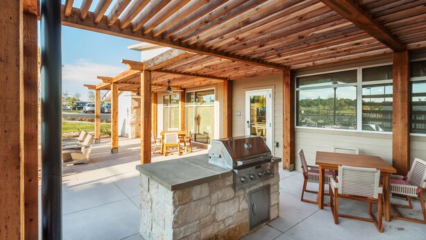 An outdoor patio with a stone barbecue and wooden furniture. - Residence Inn by Marriott Austin Airport (Austin)