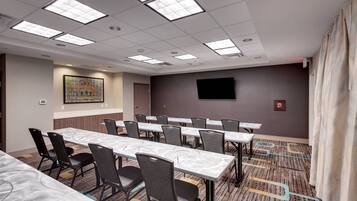 A conference room with long tables, chairs, a flat-screen TV, and a patterned carpet.