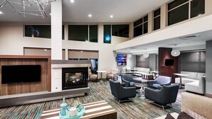 A spacious lobby with a flat-screen TV, a fireplace, comfortable seating, and a patterned carpet. - Residence Inn by Marriott Austin Airport (Austin)