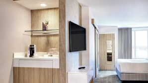 Ett modernt hotellrum med en väggpanel i trä, en platt-TV, en kaffebryggare och en säng med ett randigt sänggavel.