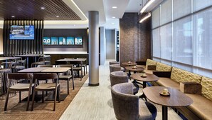 En modern hotellobby med en sittgrupp, bord och en tv-skärm som visar en meny.