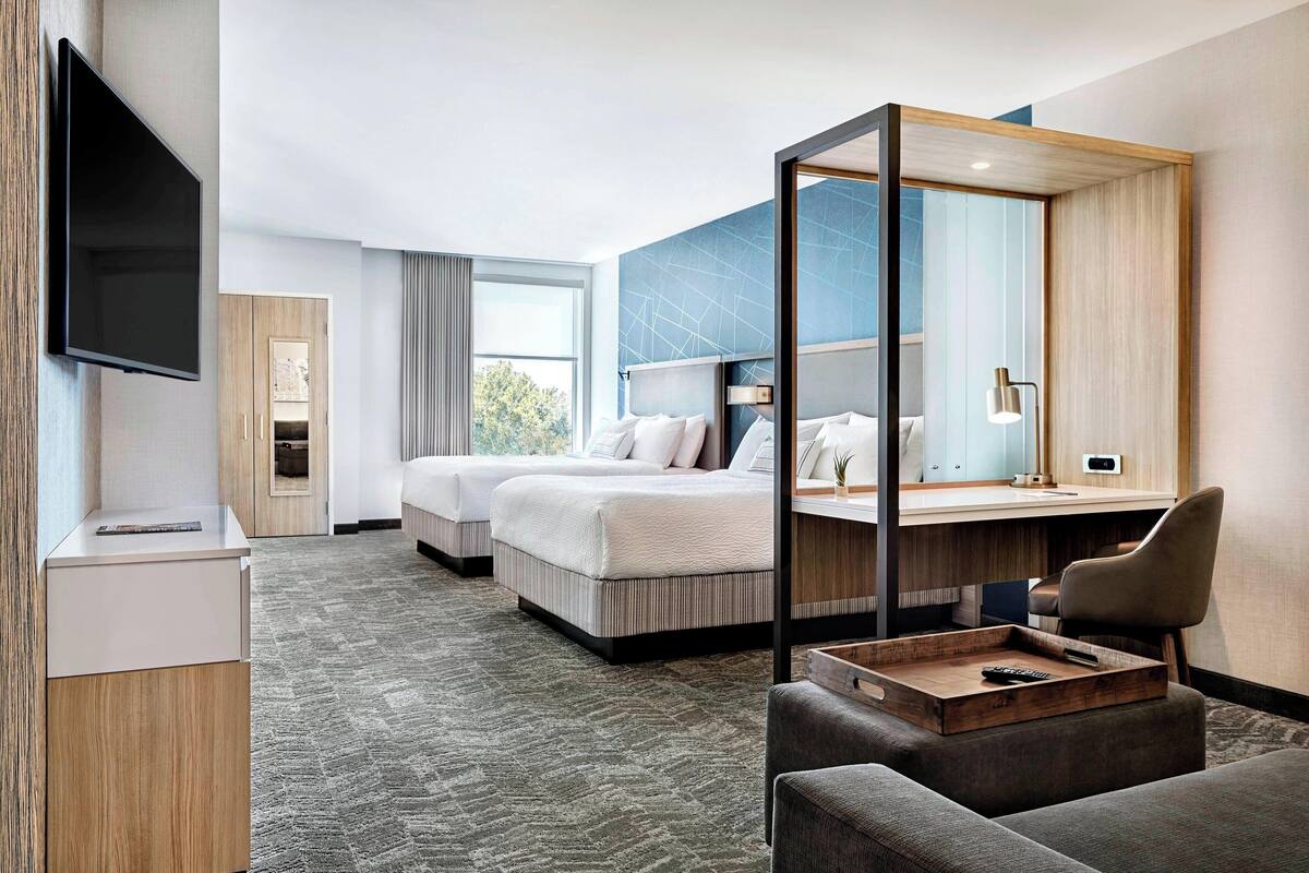 A hotel room with a large bed, a desk, a chair, a TV, and a window.