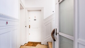 Um corredor estreito com piso de madeira, paredes brancas e uma porta com o número 1.
