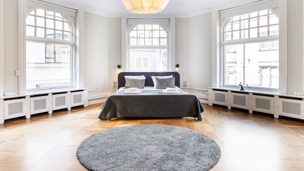 Quarto com uma cama grande, duas janelas, um radiador e uma luz de teto.