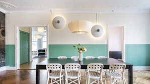 Uma sala de jantar com uma mesa comprida, cadeiras brancas e um vaso de flores.
