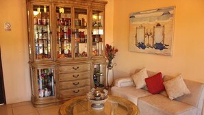 A living room with a beige sofa, a glass-top coffee table, a wooden cabinet with glass doors, and a painting on the wall. - Hotel Palacio Real Granada (Granada)