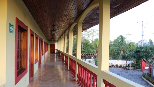 A covered corridor with red balustrades and tiled flooring, leading to a courtyard with potted plants and a fountain. - Hotel Palacio Real Granada (Granada)