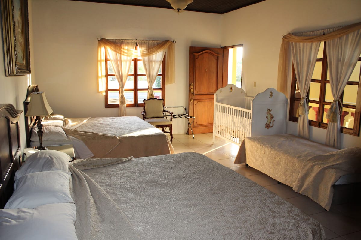 A room with two beds, a chair, a crib, and a door.