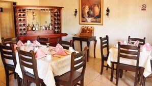 A dining area with wooden chairs and tables, a wine rack, and a painting on the wall. - Hotel Palacio Real Granada (Granada)