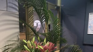 A wooden table with a dark blue vase containing pink lilies and green foliage. - SmartStay Melbourne (Windsor)