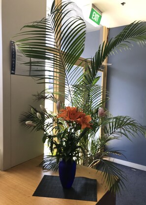 A reception area with a blue vase containing orange flowers, a wooden reception desk, and a door with an 'EXIT' sign. - SmartStay Melbourne (Windsor)