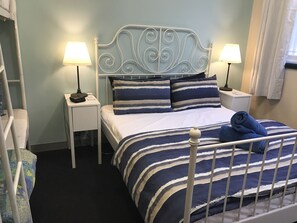 A neatly made bed with striped bedding, two bedside lamps, and a headboard with decorative scrollwork. - SmartStay Melbourne (Windsor)