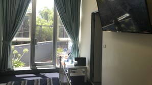 A room with a bed, a desk, a chair, a TV, and a balcony with curtains. - SmartStay Melbourne (Windsor)