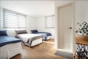 A bedroom with two beds, a door, and a small table with a plant. - Welcome House (Suwon)