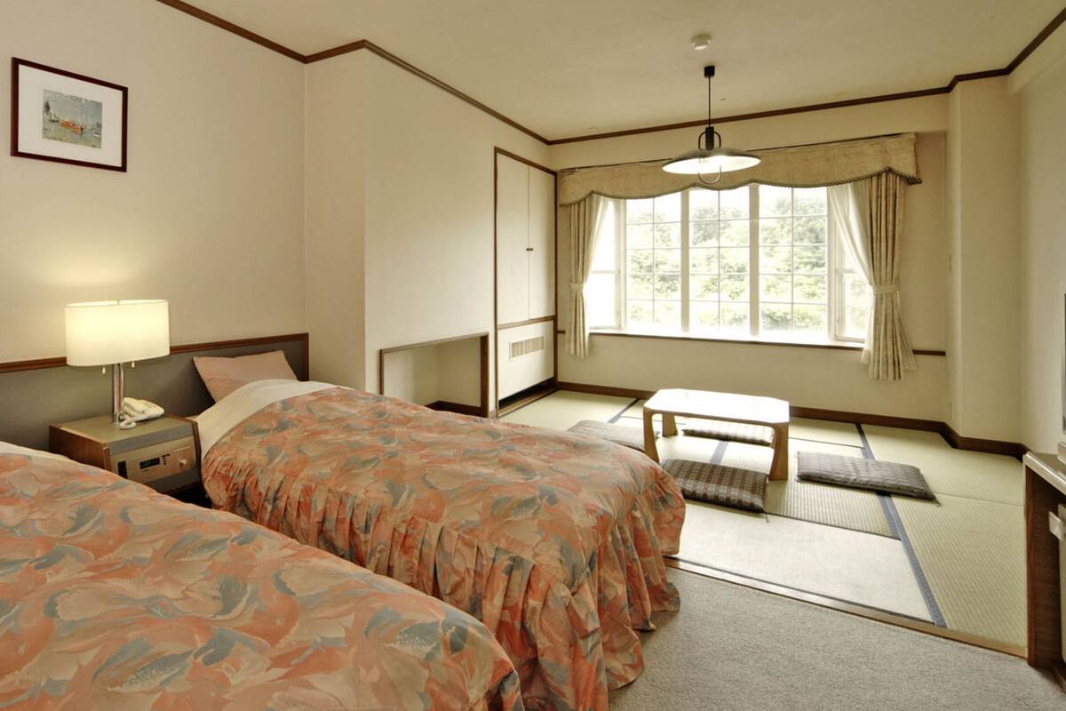 A hotel room with two beds, a desk, a television, and a window with curtains.