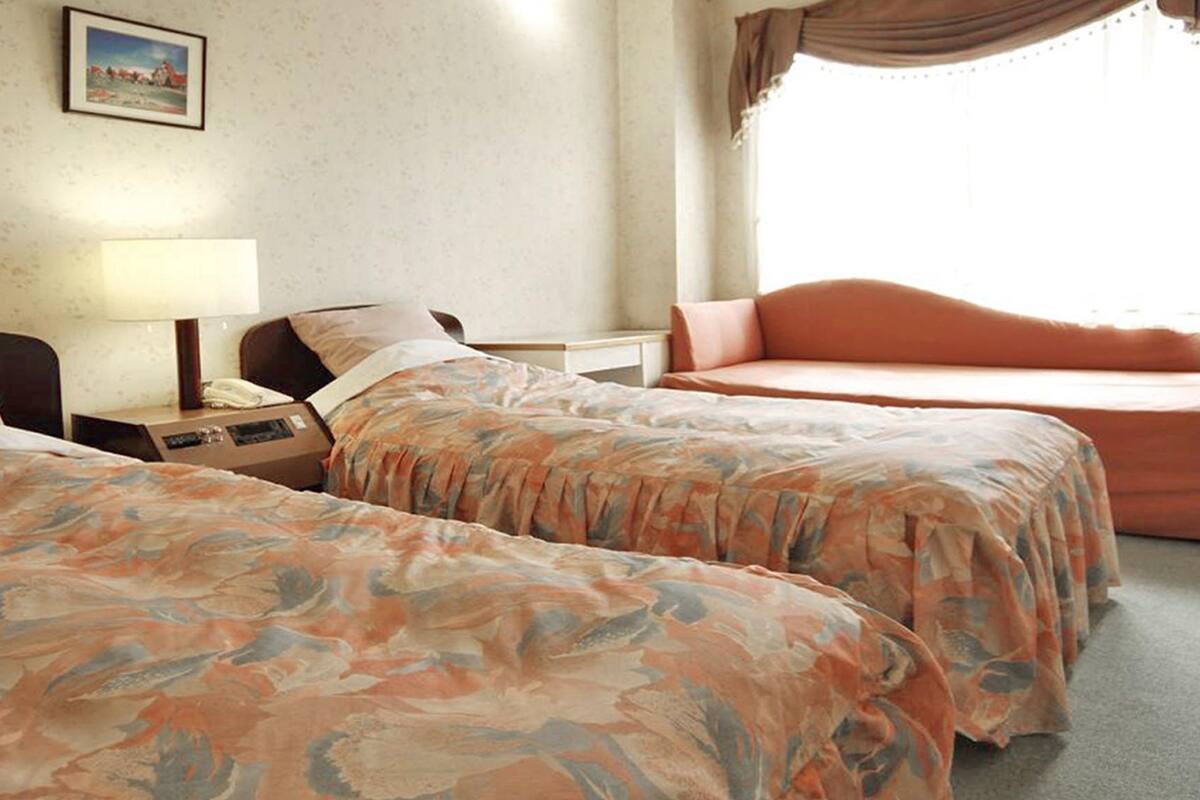 A hotel room with two beds, a nightstand with a lamp, a telephone, and a picture on the wall.
