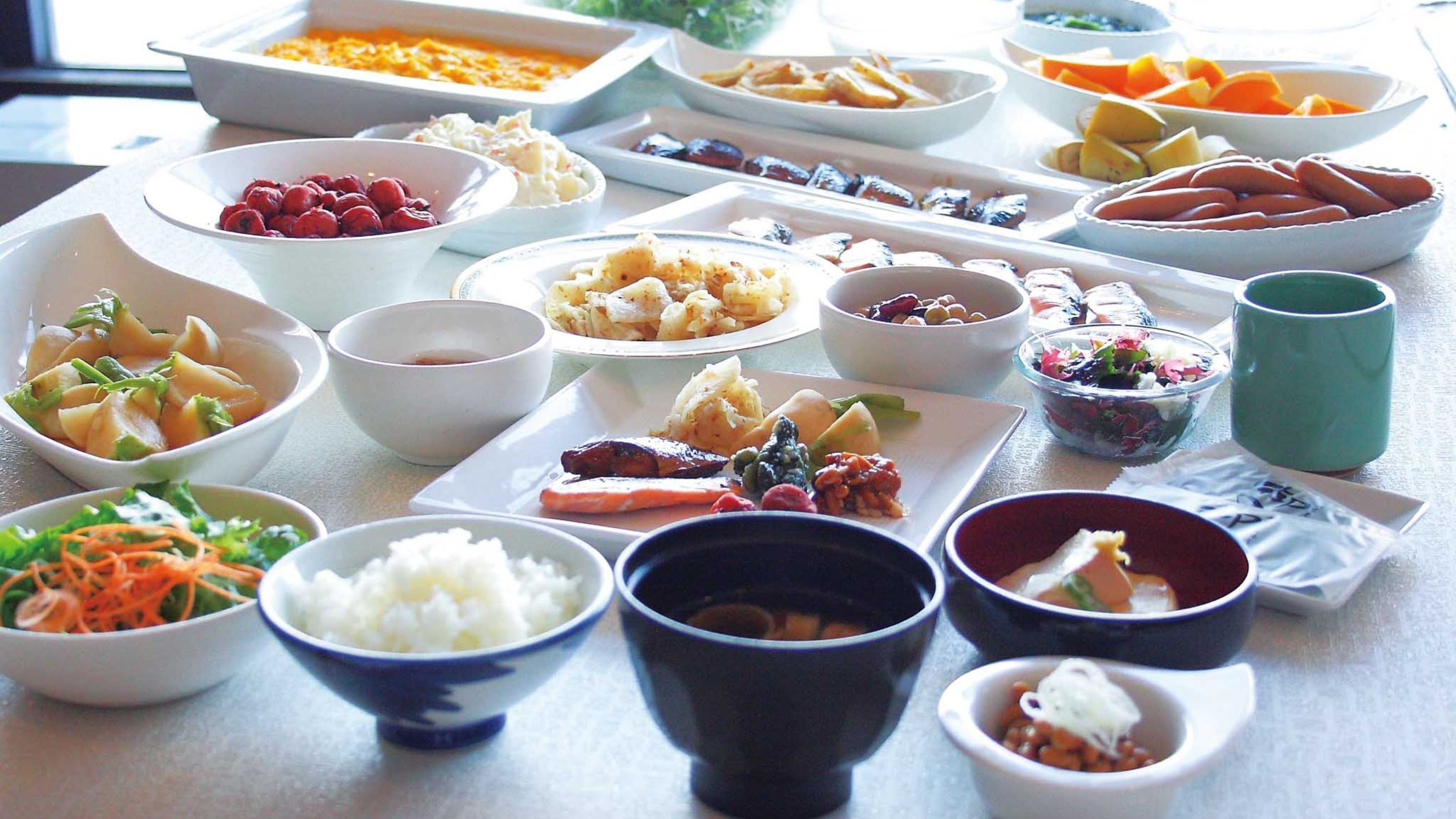 A table with various dishes including sushi, vegetables, and a green cup.