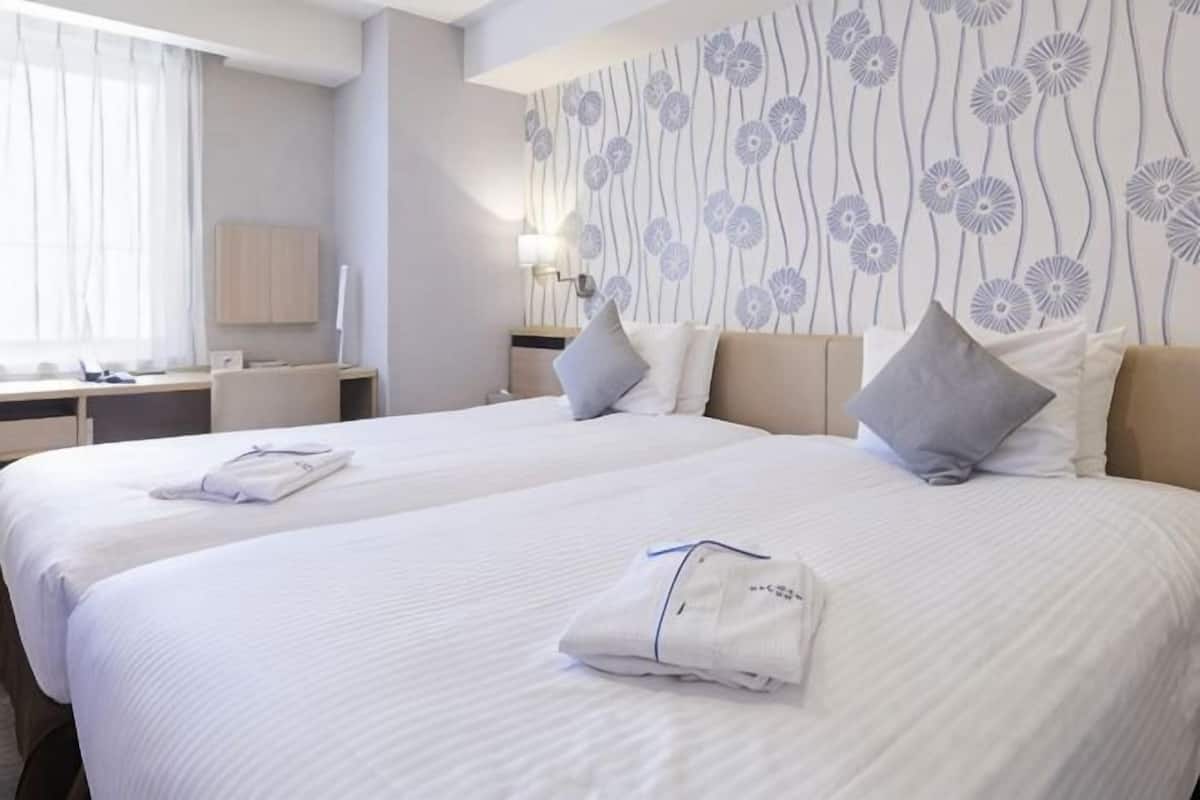 A hotel room with two beds, a desk, and a wall with a floral pattern.