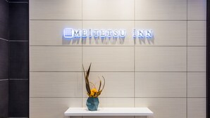 A reception area with a modern design, featuring a neon sign that reads "MEITETSU INN" and a decorative vase with yellow flowers on a white shelf. - Meitetsu Inn Hamamatsucho (Tokyo)