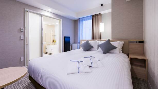 A hotel room with a neatly made bed, a bedside table, a small desk, and a view of the bathroom. - Meitetsu Inn Hamamatsucho (Tokyo)